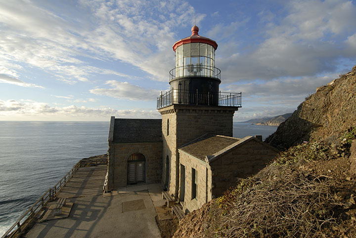 a stone lighthouse with a red rounded roof sits on a cliffside